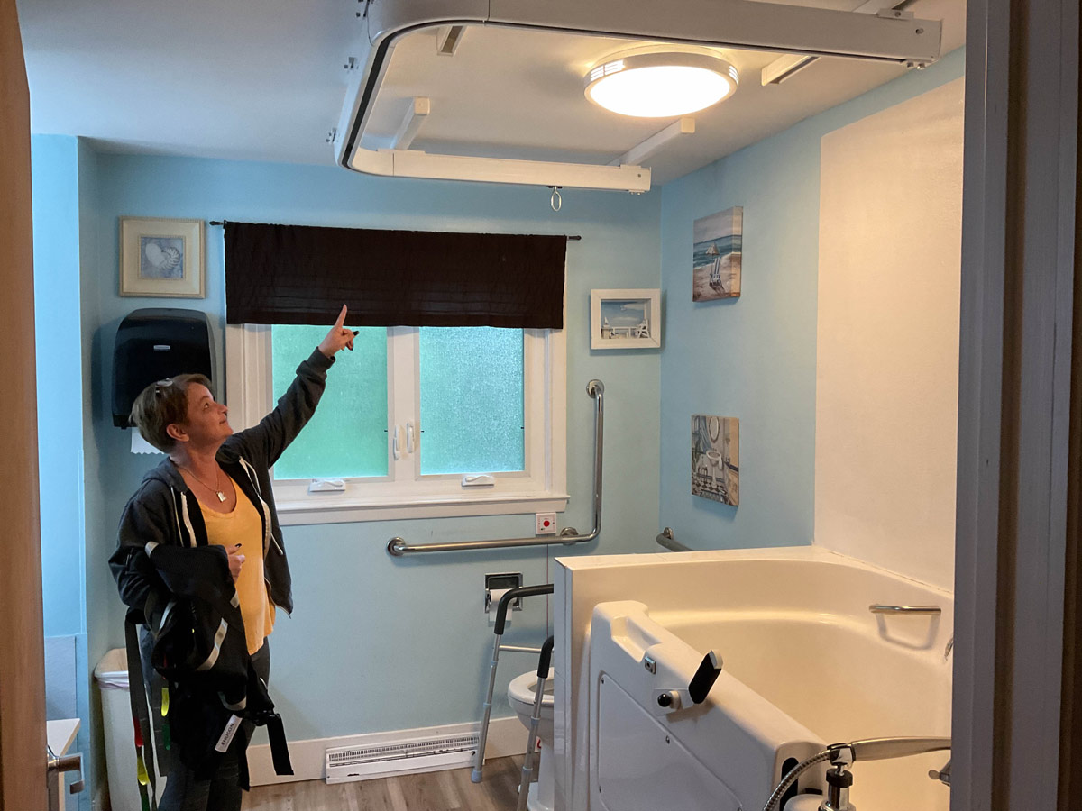 Woman in Accessible bathroom pointing to support track on the ceiling
