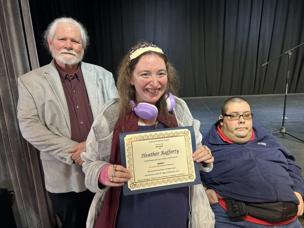 Self-advocacy graduate Heather Rafferty holds a certificate on-stage alongside Dan Flanigan.