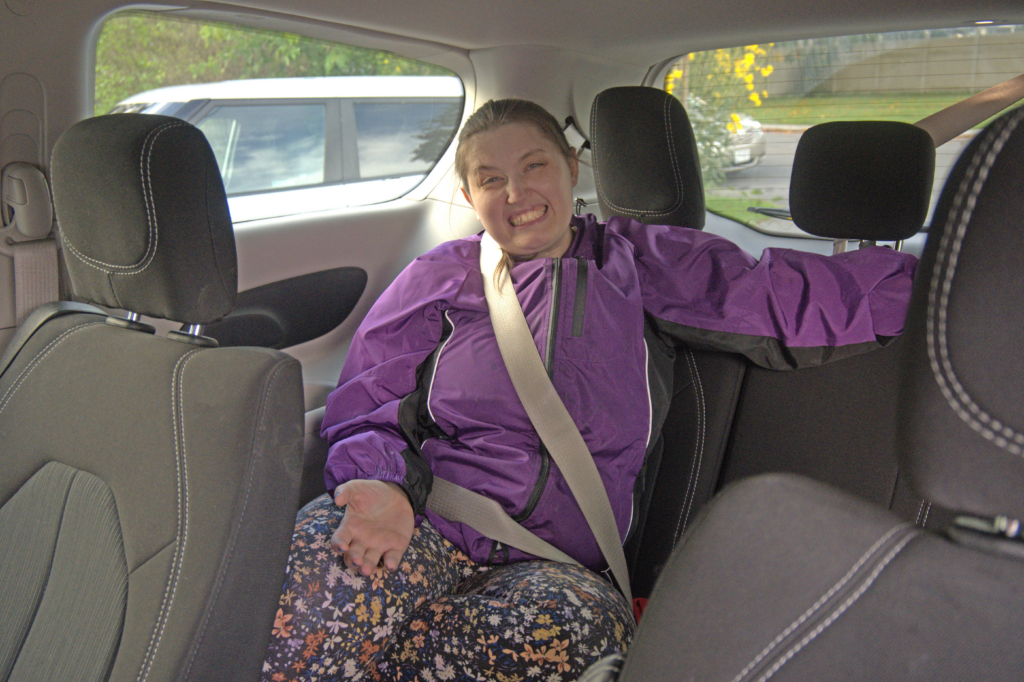 Unity House resident Kristen Rogalski, of Auburn, sits in the back of a transport van on her way to Auburn Day Hab. She is wearing a purple windbreaker and floral leggings.