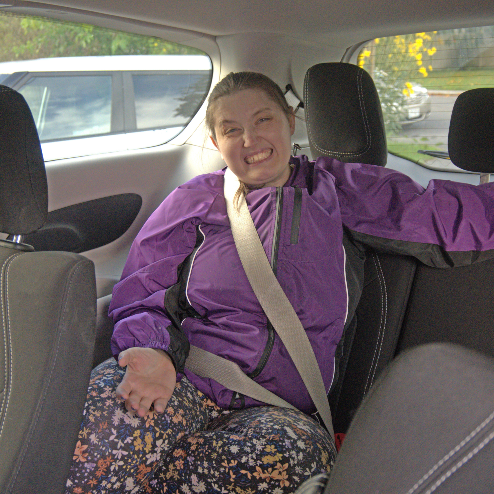 Unity House resident Kristen Rogalski, of Auburn, sits in the back of a transport van on her way to Auburn Day Hab. She is wearing a purple windbreaker and floral leggings.